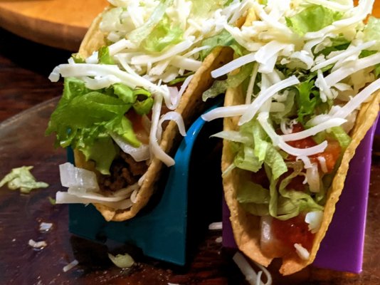 Tacos with seasoned meat, lettuce, chopped onion, taquera sauce, shredded cheddar, and crème f...jpg